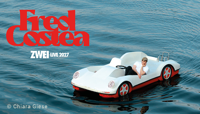 Fred Costea sitzt in einem Tretboot, das wie ein weißer Porsche mit rotem Unterboden aussieht. Er hat das Kinn in die Hand gestützt und schaut nachdenklich auf das Wasser.
